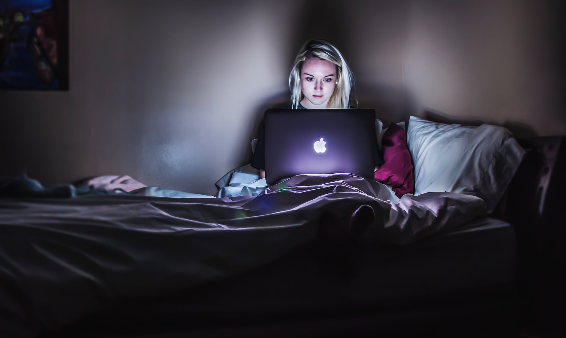 woman sitting in the dark in bed with laptop