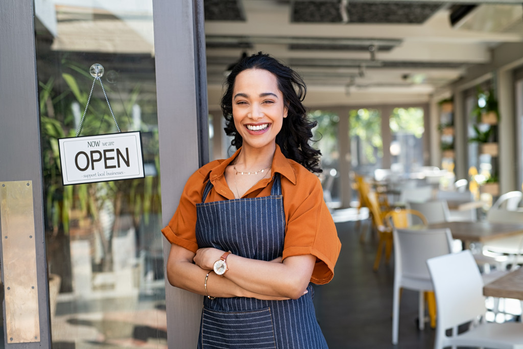 Young business woman wearing apron standing with open sign at entrance