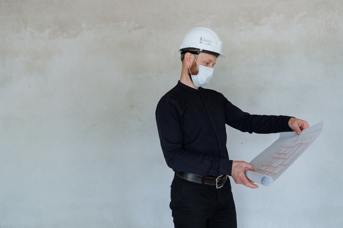 A Man Wearing a Hard Hat and a Face Mask while Looking at a Blueprint