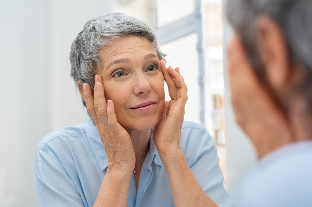 Old woman checking her skin on the mirror